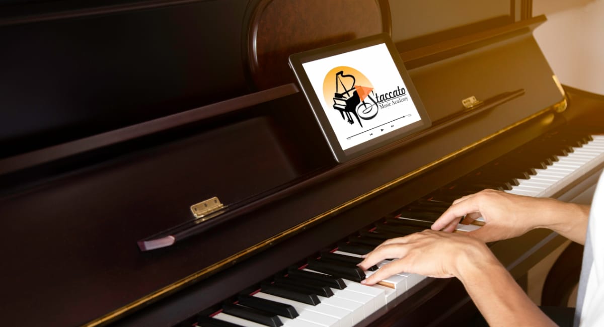 A tablet showing the Staccato video course on a piano music stand